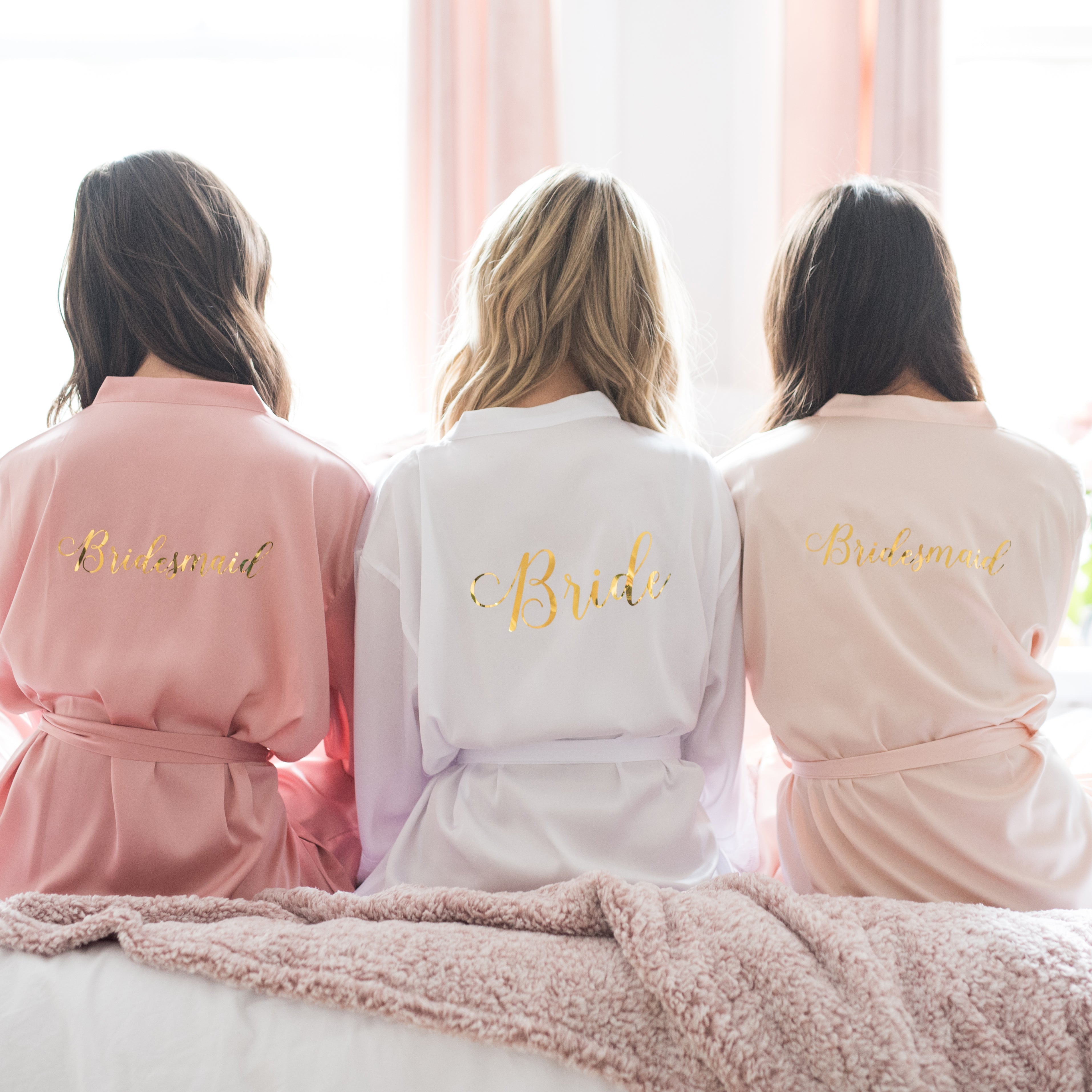 Bridal Party Robes - Three beautiful models dressed in white, blush and dusty rose satin lace bridal party robes with monogram design on the back of the robe in preparation for a bachelorette party, wedding or any fun occasion.