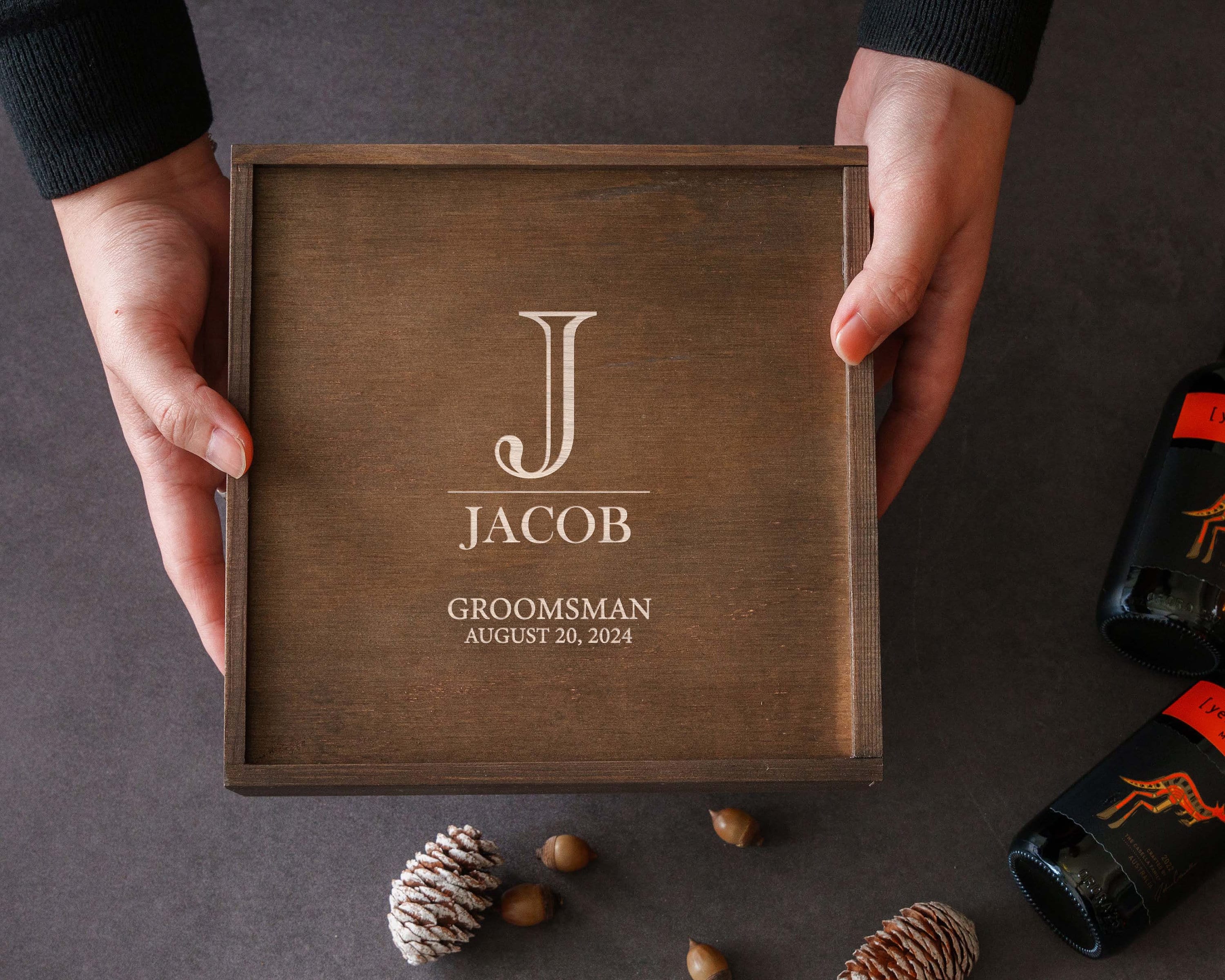 a person holding a box of wine next to pine cones