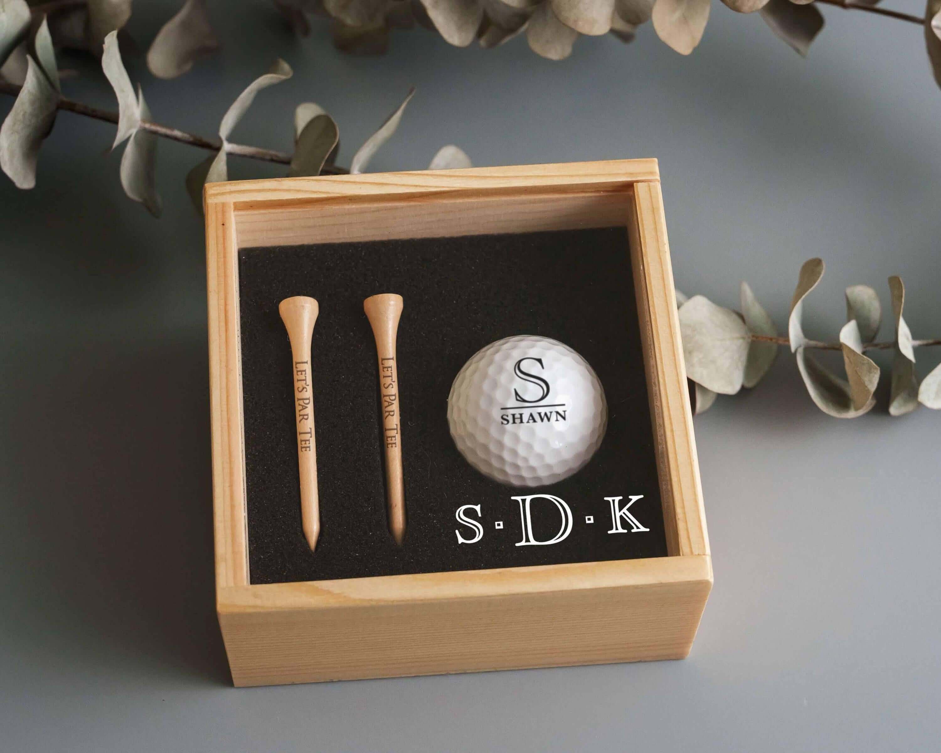 a golf ball and two tees in a wooden box